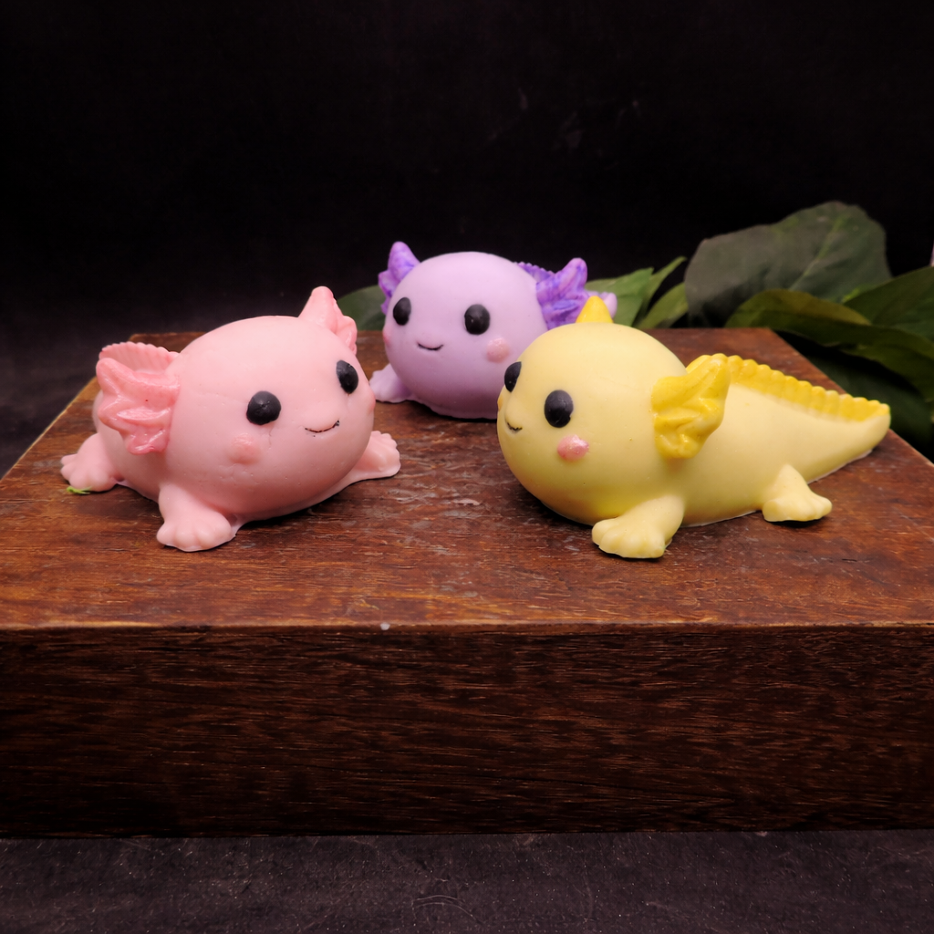 Individually handcrafted pink axolotl goat milk soap displayed on a rustic wooden block with warm lighting and dark background facing each other