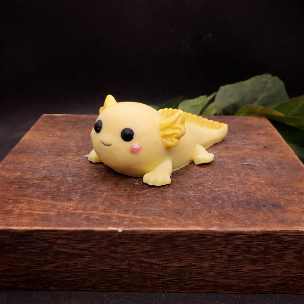 Individually handcrafted yellow axolotl goat milk soap keepsake displayed on a wooden block with warm lighting and dark background