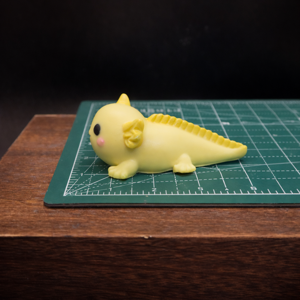 Side profile of an individually handcrafted yellow axolotl goat milk soap keepsake resting on a  cutting mat to show size