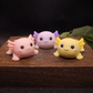 Three colorful axolotl figurines on a wooden surface with a dark background keepsake unique gifts