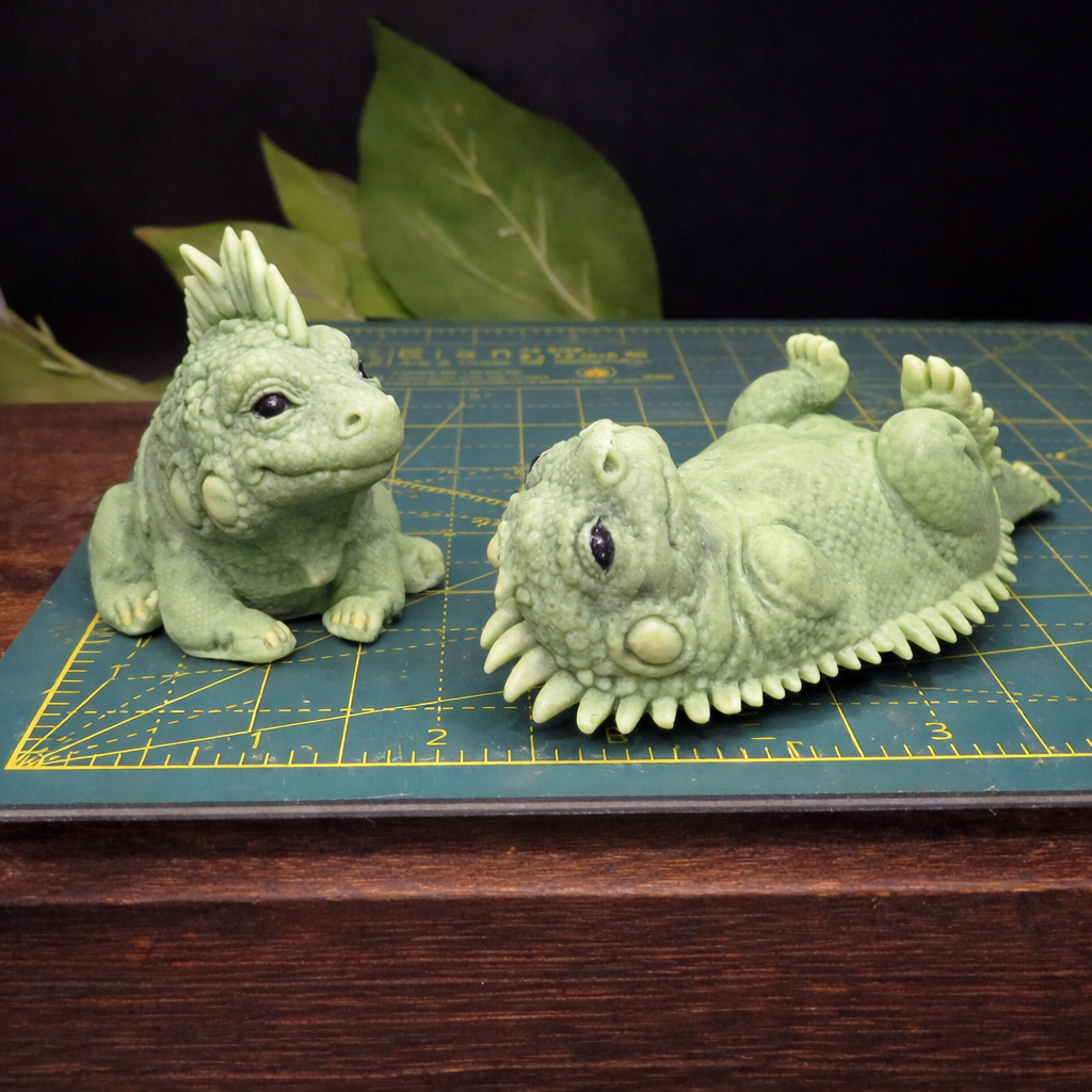 Two handmade iguana goat milk soaps photographed on a cutting mat to show accurate size, scale, and surface detail.