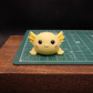 front view Individually handcrafted yellow axolotl goat milk soap keepsake displayed on a  cutting mat to show size